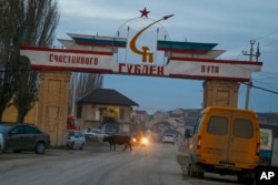 FILE - An entrance to the village of Gubden with a sign reading "Happy Travel. Gulden" is decorated with banner in colors of Russian and Dagestani flags, in the village of Gubden, Dagestan, Russia, Nov. 15, 2015.
