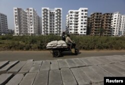 FILE- Laborers transport cement bags onto an improvised motorized rickshaw at the construction site of a residential complex on the outskirts of Kolkata, India, Jan. 23, 2016.