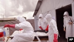 Health workers wearing Ebola protective gear remove the body of a man they suspect died from the Ebola virus, at a USAID, American aid Ebola treatment center on the outskirts of Monrovia, Liberia, Nov. 28, 2014.