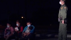 n this March 24, 2021 photo, a migrant man, center, holds a child as he looks at a U.S. Customs and Border Protection agent at an intake area after crossing the U.S.-Mexico border, early Wednesday, March 24, 2021, in Roma, Texas.