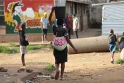 In this Monday, April 6, 2020 photo, a woman carries a her baby and a bucket of water in Harare. Lockdowns imposed to curb the coronavirus’ spread have put millions of women in Africa, Asia and elsewhere out of reach of birth control. (AP Photo/Tsvangiray