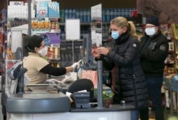 Supermarket employees and customers wear protective masks in a shop in Vienna, Austria, Wednesday, April 1, 2020.