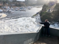 In this Jan. 11, 2020 photo residents watch as an extreme high tide rolls in and floods parts of the harbor in Depoe Bay, Oregon, USA. (AP Photo/Gillian Flaccus)