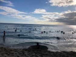 In this photo taken May 13, 2020 in Honolulu, people are in the water at a Waikiki beach. A group of people are helping track down violators of a 14-day quarantine on travelers arriving to Hawaii. (AP Photo/Jennifer Sinco Kelleher)