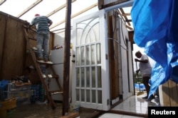 Lourdes Rodriguez (R) cleans while her husband repairs the roof of their home, damaged by Hurricane Maria in Maunabo, Jan. 27, 2018.