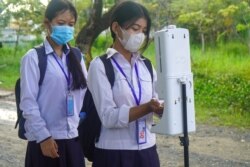 សិស្ស​សាលា វាស់​កំដៅ​ និង​បាញ់​អាល់កុល​ ដោយ​ភ្ជាប់​ជាមួយ​បណ្ណ​ចាក់​វ៉ាក់សាំង​ មុន​ដើរ​ចូល​ថ្នាក់​រៀន​ រាជធានី​ភ្នំពេញ​ ថ្ងៃ​ទី១​ ខែ​វិច្ឆិកា​ ឆ្នាំ​២០២១។​ (ហ៊ាន សុជាតា​/វីអូអេ)​