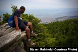 A hiker admires the view, as the parkway winds around mountains in the distance.
