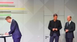 German Chancellor-designate Olaf Scholz, SPD, right, and Economy and Climate Minister-designate Robert Habeck, Greens, center, chat while Finance Minister-designate Christian Lindner, FDP, signs a coalition deal in Berlin, Dec. 7, 2021.