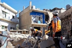 This June 26, 2018, photo, provided by Nabaa Media, a Syrian opposition media outlet, shows civil defense workers and civilians inspecting damaged buildings that were hit by Syrian government forces bombardments, in Dara'a, southern Syria.