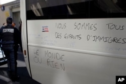 France Migrants: Police officer walks by a graffiti reading "We Are All Children of Migrants' Children, The World or Nothing" after they evacuate migrants camped out in the empty Jean Jaures school in northeast Paris, France, Wednesday, May 4, 2016.