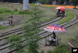 FILE - Filipino students ride a metal-wheeled cart with benches fashioned from scrap wood for 10 pesos (about US 20 cents) each for a ride along the railway in Manila, Philippines, Aug. 12, 2015. Manila and other cities are choked with construction sites for office and apartment towers. But spending on roads, railways and other unglamorous but essential infrastructure collapsed after the 1997 financial crisis and has yet to recover.