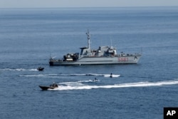FILE - An Italian Navy vessel, Italian Police on sea scooters and Coast Guard patrol on the sea in front of Taormina, Italy, May 23, 2017.