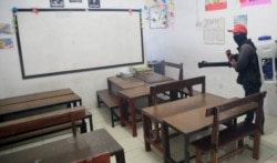 Petugas menyemprotkan cairan desinfektan di ruang kelas di sebuah sekolah di Surabaya (foto VOA/Petrus Riski).