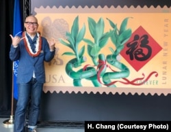 Kam Mak stands next to an image of the Year of the Dog stamp he created, which was dedicated in Honolulu. Mak is giving the friendly Hawaiian shaka sign, which means hang loose.