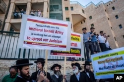 FILE - Ultra-Orthodox Jewish men wave signs, some protesting the draft, and chant outside the new U.S. Embassy in Jerusalem, May 14, 2018.