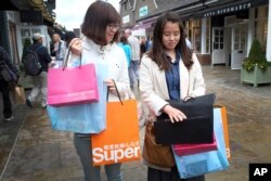 FILE - Shoppers carry designer label branded bags at a designer outlet center, in Bicester, England, Aug. 26, 2015. Chinese customers have become a powerful market force in the global trade in expensive clothes, jewelry, watches and handbags.