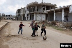 FILE - Children play near damaged buildings in the rebel-held southern town of Bosra al-Sham, Deraa, Syria, Feb. 23, 2016.