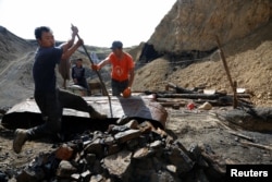 FILE - Uuganbaatar, left, and his colleagues work on extracting coal from a primitive mine in Nalaikh, one of the nine districts of Mongolian capital Ulaanbaatar, Mongolia, June 29, 2017.