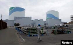 FILE - An employee of Kyushu Electric Power Co walks in front of reactor buildings at the company's Sendai nuclear power plant in Satsumasendai, Kagoshima prefecture.