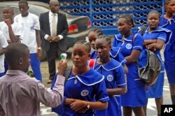FILE – A Liberian teacher takes the temperature of arriving students as part of Ebola prevention measures at BW Harris High School in Monrovia, Feb. 16, 2015.
