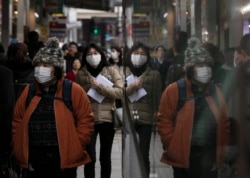 Commuters wearing protective face masks walk on a sidewalk Monday, Jan. 27, 2020, in the Shinjuku district of Tokyo. (AP Photo/Jae C. Hong)