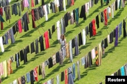 A woman walks among dresses and skirts hanging inside a stadium, in an art exhibition titled "Thinking of You" by Kosovo-born, London-based artist Alketa Xhafa-Mripa, in Pristina, June 12, 2015. Dresses and skirts donated by Cherie Blair and Rita Ora were among 5,000 pegged to clotheslines in the Kosovo stadium in an exhibit aimed at drawing attention to the stigma suffered by victims of wartime sexual violence.