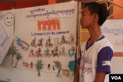 Seorang remaja di dekat karya seninya yang mengajak masyarakat untuk meningkatkan kesadaran tentang migrasi yang aman​ pada lokakarya refleksi tahunan tentang “Hasil dan Peran CYN dalam Meningkatkan Kesadaran tentang Migrasi Aman dan Pencegahan Perdagangan Manusia di Kamboja” pada 12 Juni 2015. (Foto: VOA)