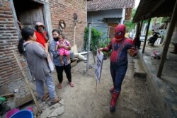 Agus Widanarko, 40, mengenakan kostum Spiderman sambil membawa spanduk saat menghibur anak-anak yang terkurung di rumah akibat pembatasan COVID-19, di Sukoharjo, Jawa Tengah, 10 September 2021. (Foto: Reuters)