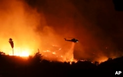 FILE - A helicopter drops water over a wildfire in Bonsall, Calif., Dec. 7, 2017.