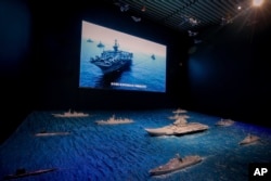 Armada Angkatan Laut AS berlayar dalam formasi di dekat model kapal induk Liaoning dengan fregat angkatan laut dan kapal selam yang dipamerkan di museum militer di Beijing, Kamis, 1 Agustus 2019. (Foto: AP)