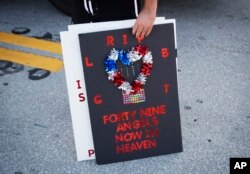 Kevin Wilson, of Orlando, stands with a sign memorializing the victims of the mass shooting while standing a few blocks from the Pulse nightclub, June 15, 2016, in Orlando, Fla.