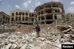 FILE - An Iranian-allied Houthi militant walks in front of a government compound, destroyed by recent Saudi-led airstrikes, in Yemen's northwestern city of Amran, July 27, 2015.