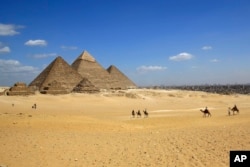 FILE - Tourists ride camels at the historical site of the Giza Pyramids in Giza, near Cairo, Apr. 9, 2015.