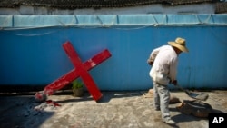 FILE - A church member shovels cement mix preparing to re-mount a cross on a Protestant church, which had been forcibly pulled down by Chinese government workers in Taitou Village, eastern China, July 29, 2015.