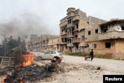 FILE - A man pulls a wheelbarrow past destroyed buildings after clashes between military forces loyal to Libya's eastern government and Islamist fighters, in Benghazi, Libya, Feb. 28, 2016.