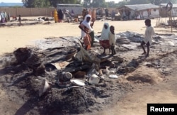 FILE - People stand amid the damage at a camp for displaced people after an attack by suspected Boko Haram insurgents in Dalori, Nigeria, Nov. 1, 2018.
