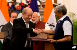 Indian Defense minister Manohar Parrikar shakes, right, hand with his French counterpart Jean-Yves Le Drian, second left, after exchanging the files of agreements on the buying of Rafale fighter jets in New Delhi, India, Jan. 25, 2016.