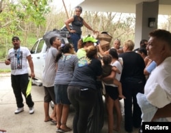 FILE - Local residents displaced by Hurricane Maria gather around a supply truck, waiting for clothing and other necessities, at a shelter in Guaynabo, Puerto Rico, Oct. 1, 2017.