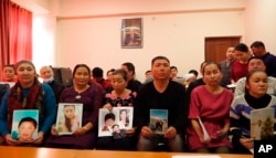 In this Dec. 7, 2018, image made from video, relatives of people missing in China's far western region of Xinjiang hold up photos at an office of a Chinese Kazakh advocacy organization in Almaty, Kazakhstan.