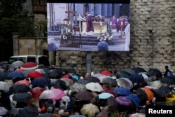 Mourners gather in the rain near a giant screen outside the Cathedral in Rouen, France, during a funeral service in memory of slain French parish priest Father Jacques Hamel at the Cathedral in Rouen, France, Aug. 2, 2016.