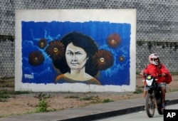 FILE - A motorcyclist rides past a mural of slain environmentalist and indigenous leader Berta Caceres in Tegucigalpa, Honduras.