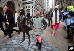 Shriya Gupta of Cherokee, N.C. strikes a pose with a statue titled "Fearless Girl", Wednesday, March 8, 2017, in New York. The statue was installed by an investment firm in honor of International Women's Day.