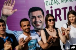 FILE - People dance in front of an election campaign poster of Selahattin Demirtas, a jailed pro-Kurdish politician and presidential candidate in Turkey's snap presidential poll, in Istanbul, June 5, 2018.