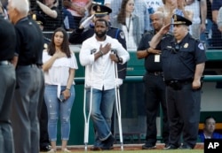 Injured Capitol Hill Police officer David Bailey, center, holds his hand over his heart during the National Anthem with U.S. Capitol Police Chief Matthew Verderosa, far right, before the Congressional Baseball Game in Washington, June 15, 2017.