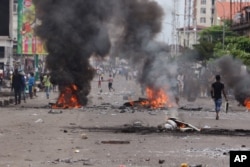 People walk near burning debris during election protests in Kinshasa, Democratic Republic of Congo, Monday, Sept. 19, 2016.