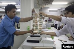 แฟ้มภาพ - พนักงานธนาคารในนครย่างกุ้งกำลังส่งมอบธนบัตรเงินจ๊าด เมื่อวันที่ 19 ต.ค. 2015