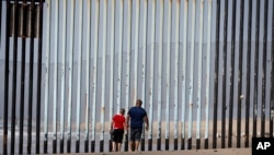 FILE - Two people walk towards metal bars marking the United States border where it meets the Pacific Ocean, in Tijuana, Mexico, March 2, 2016.