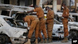 Des enquêteurs examinent une voiture brûlée devant le Splendid Hotel à Ouagadougou, au Burkina Faso, après un attentat terroriste le dimanche 17 janvier 2016.