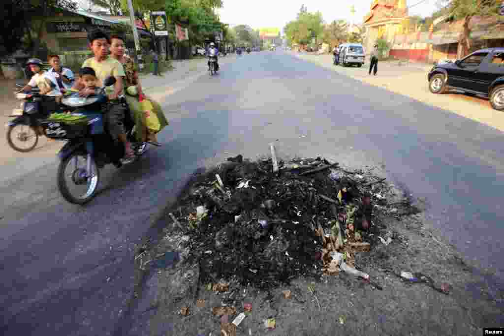 2013年3月22日，在密铁拉镇，人们骑着轻骑摩托经过两名死于冲突者的尸体。