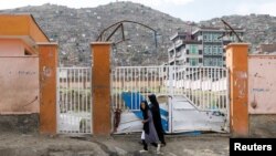 ស្ត្រីម្នាក់ដើរជាមួយក្មេងស្រីកាត់របងសាលារៀនដែលរងការបំផ្ទុះគ្រាប់បែកក្នុងរថយន្តនៅទីក្រុងកាប៊ុល ប្រទេសអាហ្វហ្កានីស្ថាន កាលពីថ្ងៃទី ១០ ខែឧសភា ឆ្នាំ ២០២១។